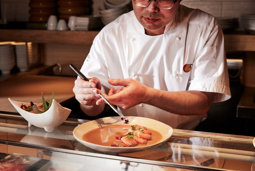 A chef carefully placing a garnish on a sushi dish with a pair of culinary tweezers.