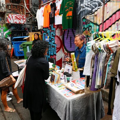 A stallholder in front of the colourful graffiti wall at Melbourne's Section 8, selling clothes and artwork.