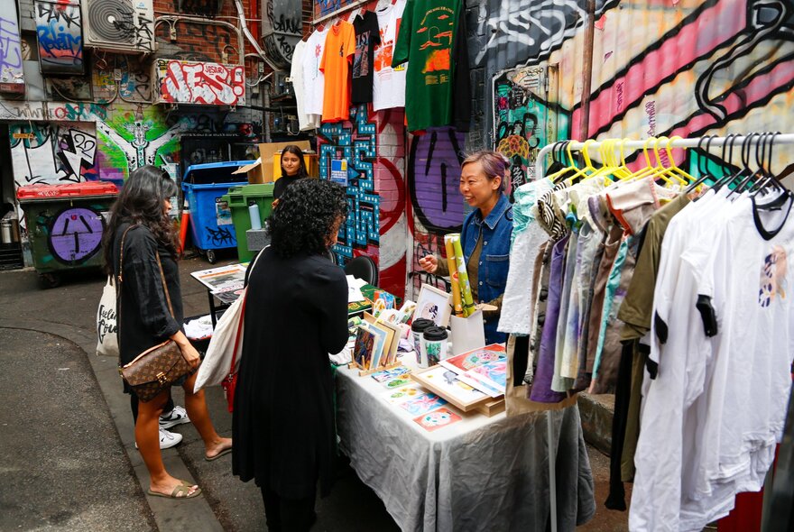 A stallholder in front of the colourful graffiti wall at Melbourne's Section 8, selling clothes and artwork.