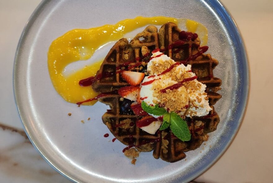 Looking down at a waffle served with ice cream and berries on a white plate.