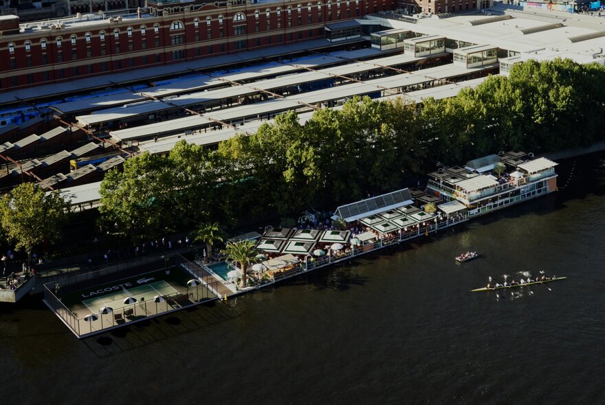 An aerial view of a floating bar and tennis court on the Yarra River next to Flinders Street Station in Melbourne.