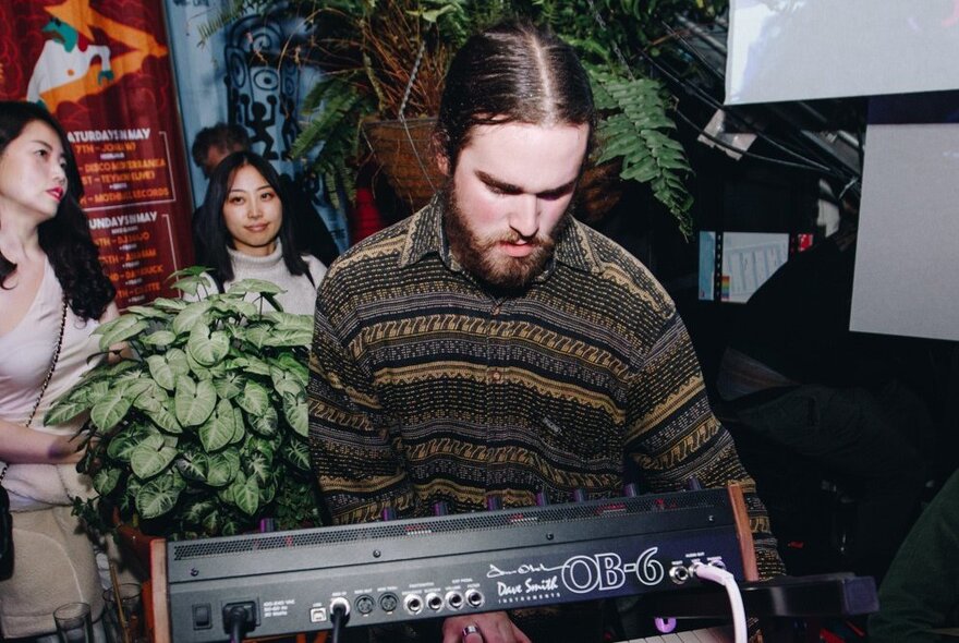 A musician wearing a patterned shirt, playing the keyboard.
