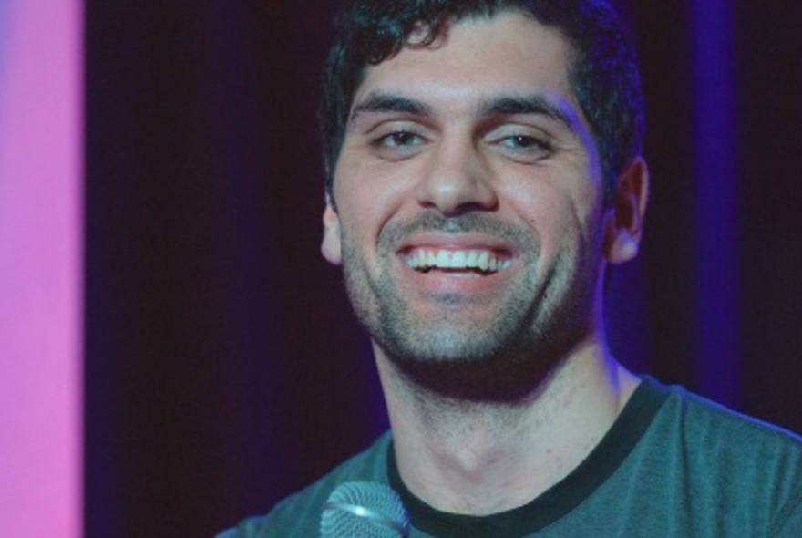 Comedian, Elijah Dries, smiling with a dark blue and purple background.