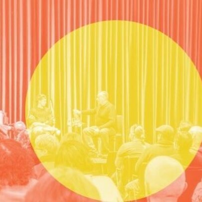 A brightly lit stage with a curtain as a backdrop, with three people in a panel discussion seated facing an audience; there is large yellow circle superimposed over the orange coloured image. 