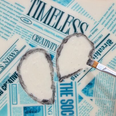 A handing using a brush to paint designs onto white chocolate so that is resembles a newspaper.