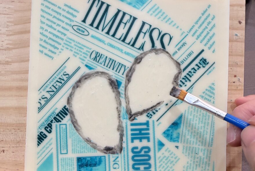 A handing using a brush to paint designs onto white chocolate so that is resembles a newspaper.