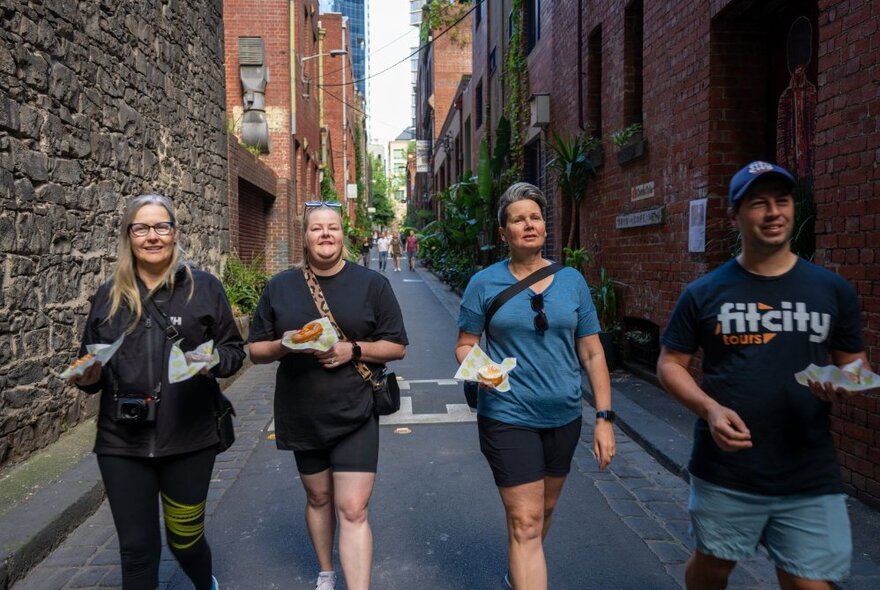 Three people walking with a Fit City tour guide through a narrow lane in central Melbourne with brick buildings on either side.