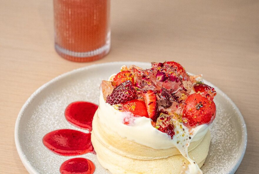 Souffle-style fluffy pancakes on a plate with berries and cream, a drink cut off in the background. 