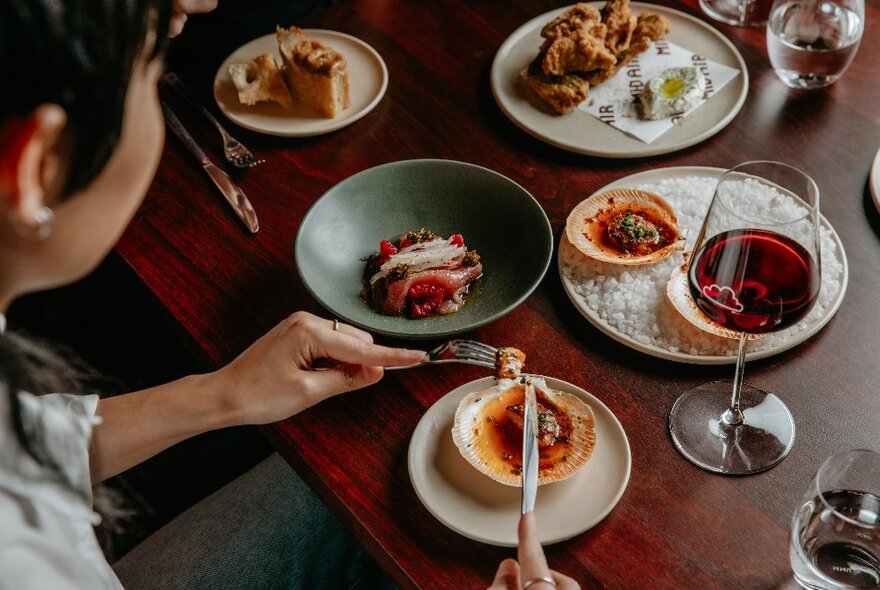 A diner enjoying various plates of food served with wine on a wooden table.