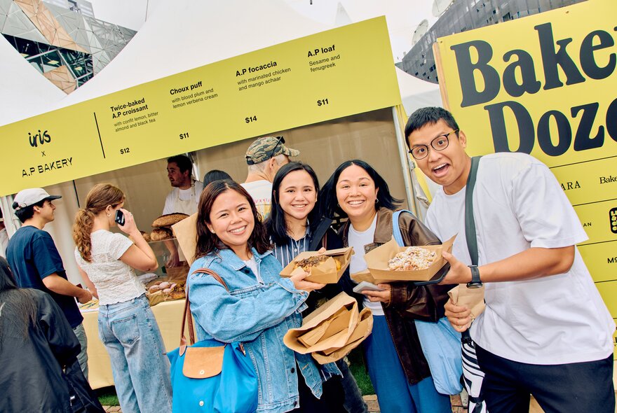 People holding loaves of bread outside a bakery stall with signage.