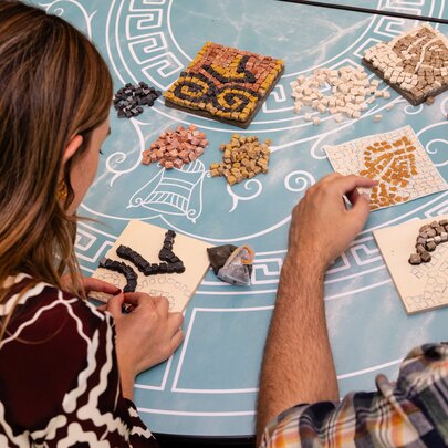 Looking over the shoulders of two people doing a craft activity on a blue tablecloth. 