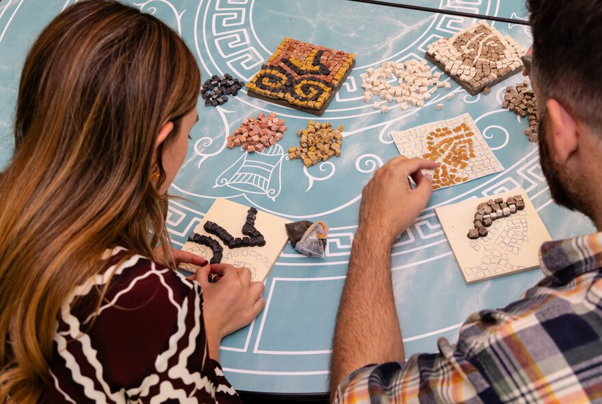 Looking over the shoulders of two people doing a craft activity on a blue tablecloth. 