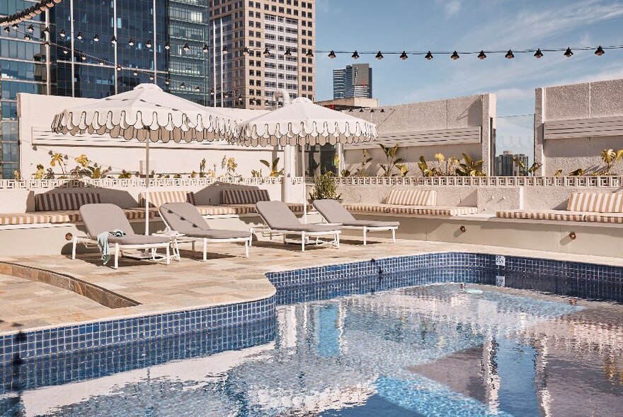 Rooftop pool with shade umbrellas, loungers and party lights with city views.