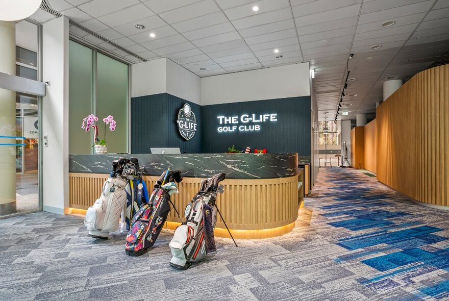 The entrance to G-Life Golf Club, an indoor golf-simulator, with three golf bags resting against the curved timber reception desk.