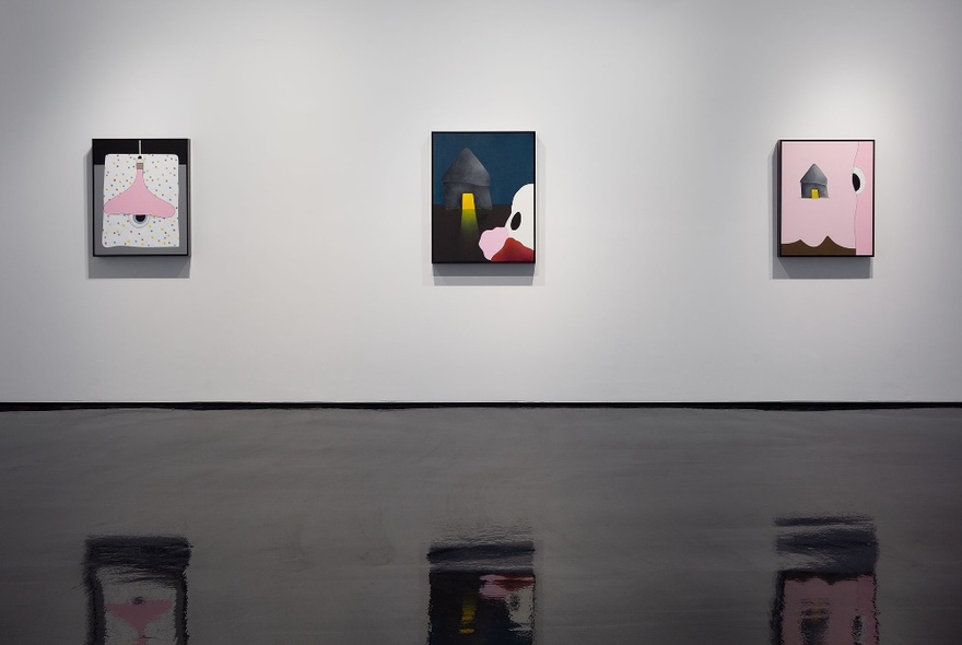 Three abstract paintings hanging on a white gallery wall, reflected in the shiny black floor.