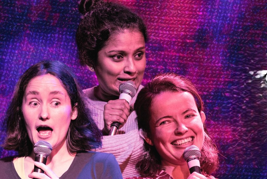 Three female comedians speaking into microphones with varied facial expressions.