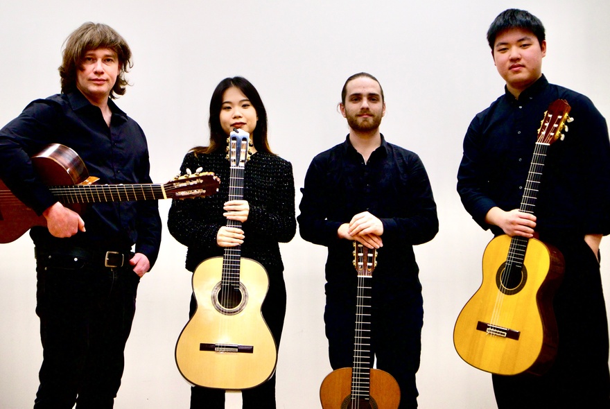 Four musicians holding guitars, dressed in black.