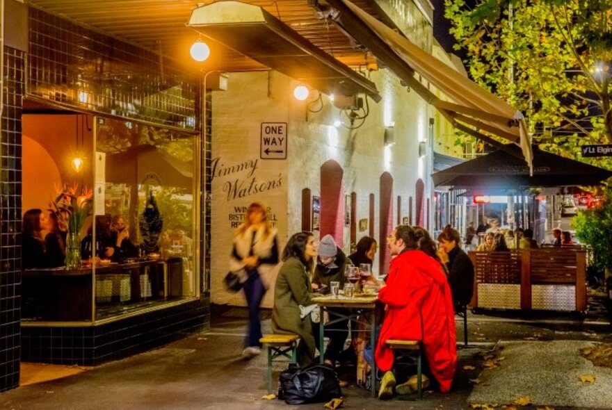 People dining outside a warmly lit cafe at night.