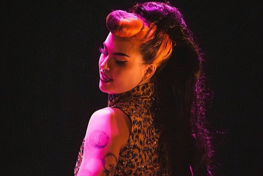 A burlesque performer wearing a leopard print top and a long purple ponytail in her hair.