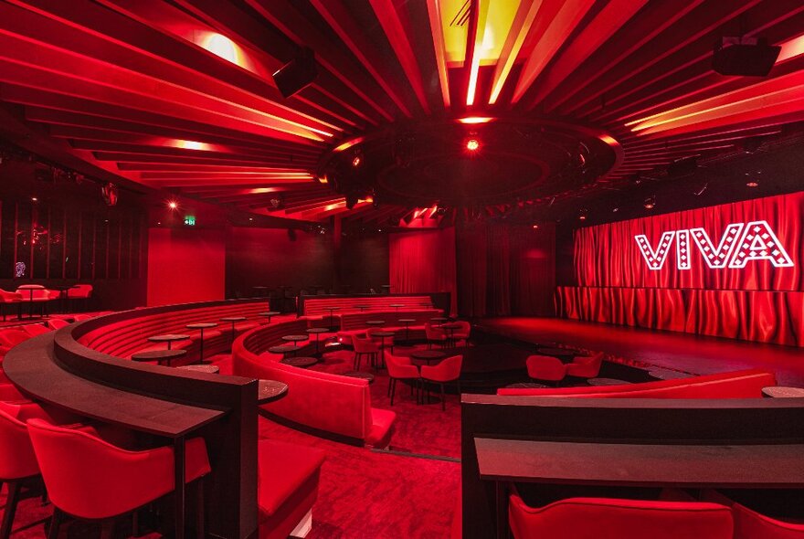 The red interior of the cabaret venue Viva, with a central stage surrounded by curved rows of seating, each with small tables nearby.