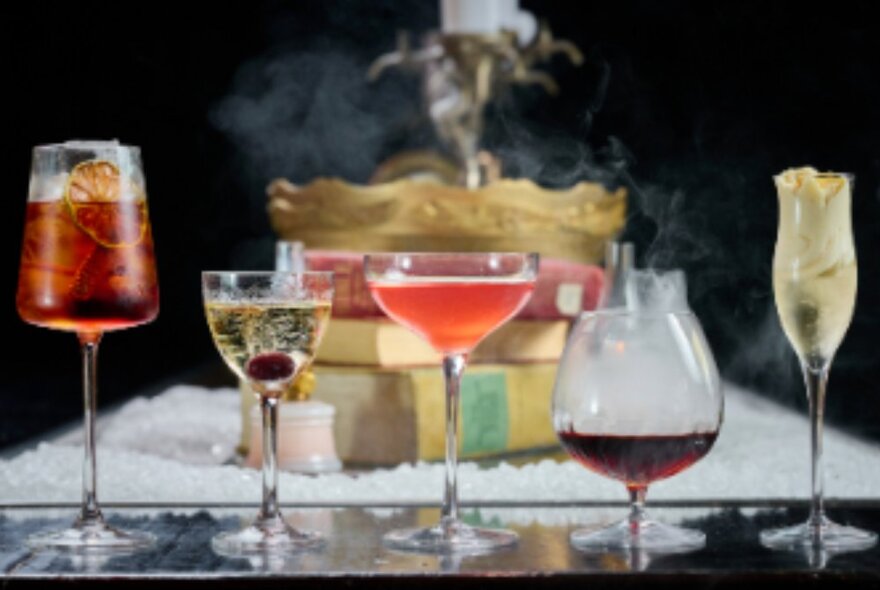 Five cocktails in different shaped glasses on a bar.