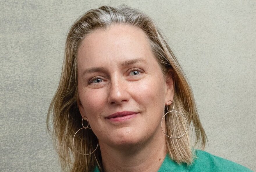 A headshot of a woman in a green top with hoop earrings, smiling. 
