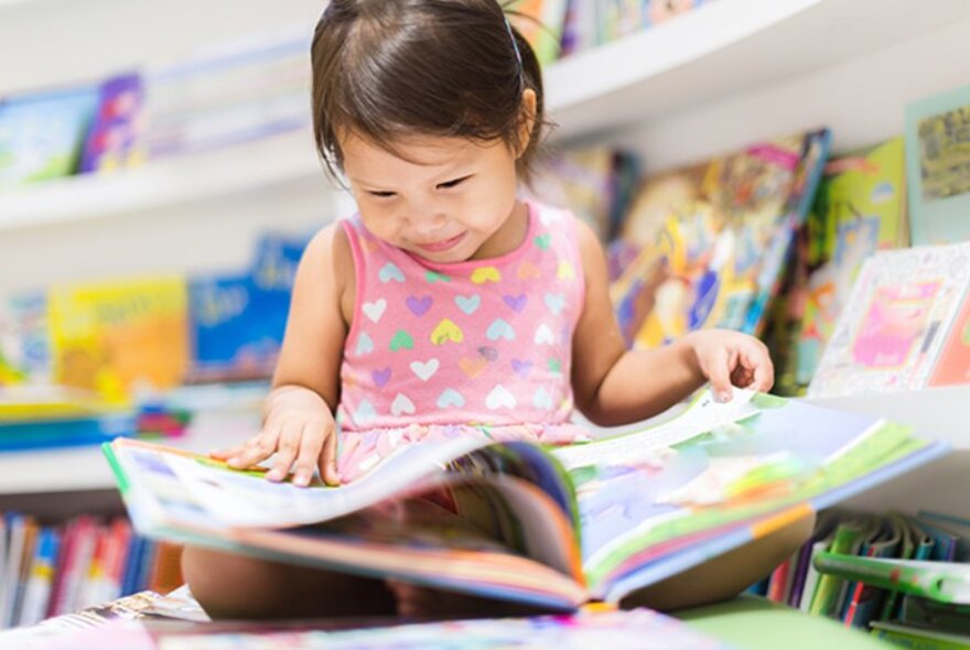 A small girl looking through a picture book in a library.