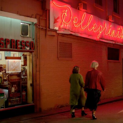 Women walking past a cafe with a neon sign at night.