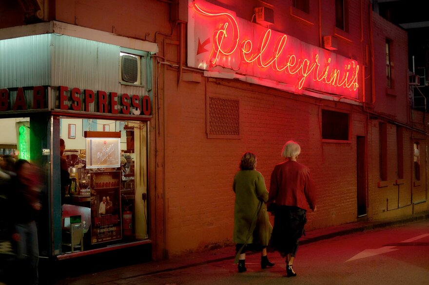 Women walking past a cafe with a neon sign at night.