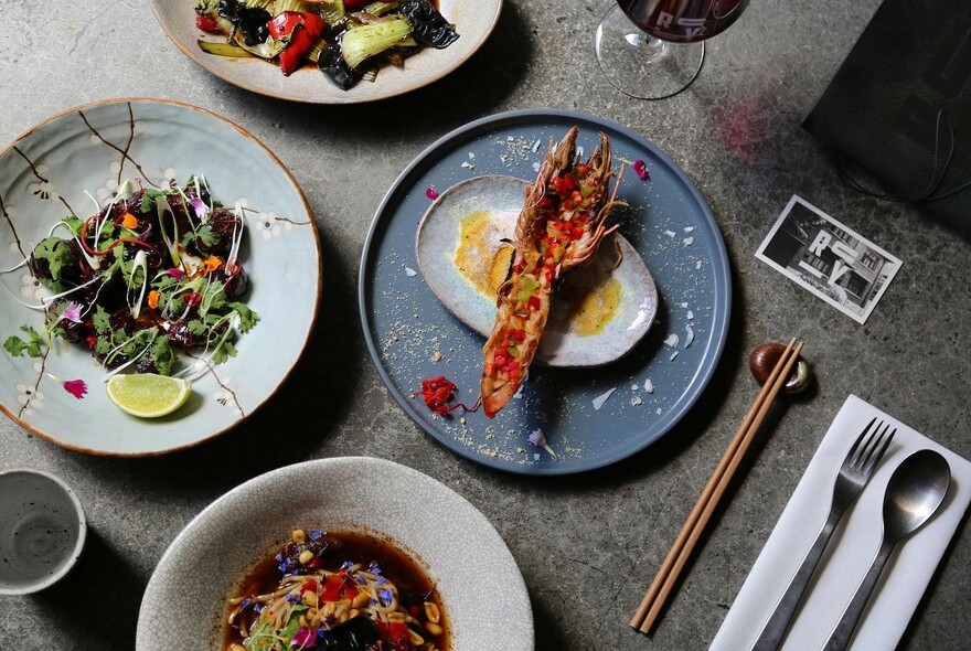 Chopsticks and cutlery next to an assortment of dishes including lobster and salads.