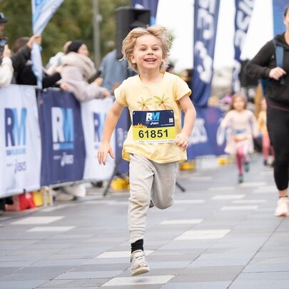 A young boy running in the kids dash at the Run Melbourne event, a parent behind him.