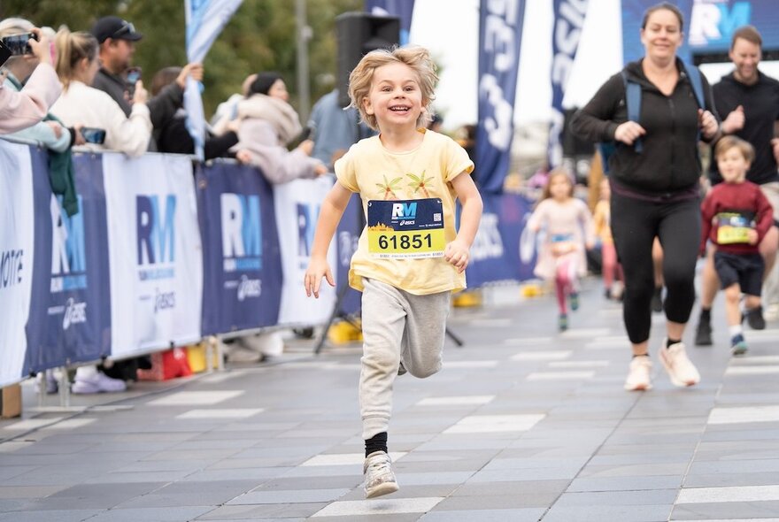 A young boy running in the kids dash at the Run Melbourne event, a parent behind him.