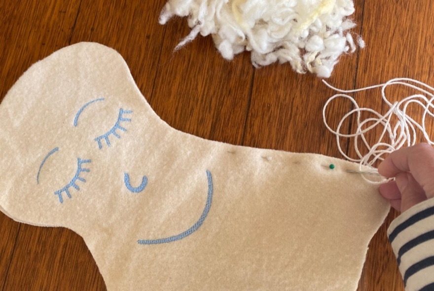 A piece of flat white wool, with thread, and stuffing, ready to be sewn into a plush soft angel.