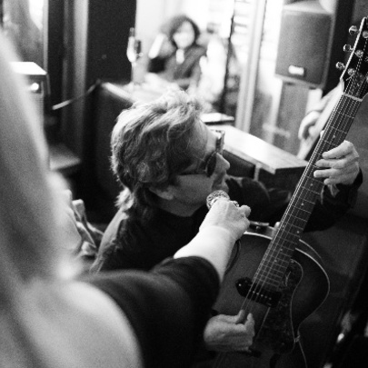 Black and white image of person playing an acoustic guitar while another individual holds a microphone for them.