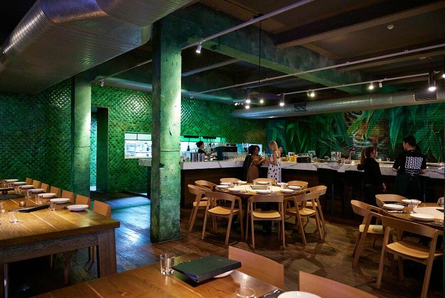 A green restaurant with timber tables and a leafy mural.