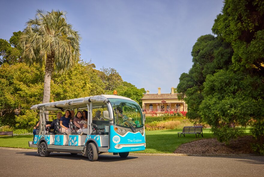 The open-sided Explorer Bus at Royal Botanic Melbourne Gardens on a path with the gardens in the background.