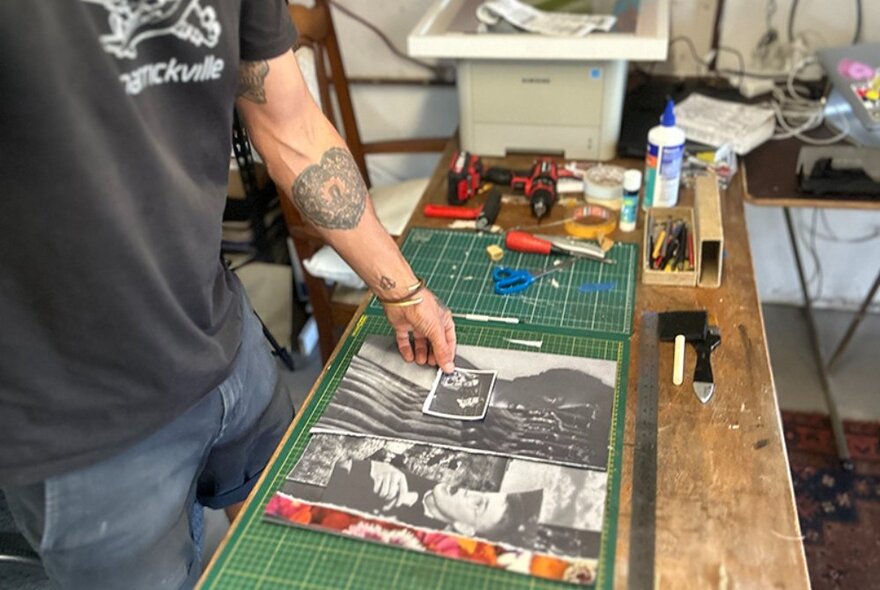 Artist piecing together a collage artwork at a workshop desk.