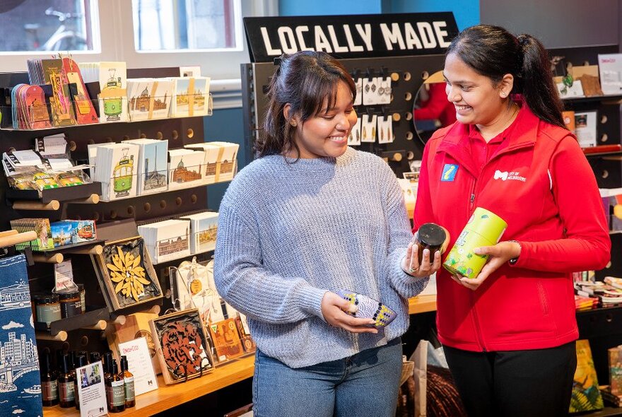 A volunteer in a tourist info centre showing gift products to a smiling customer.