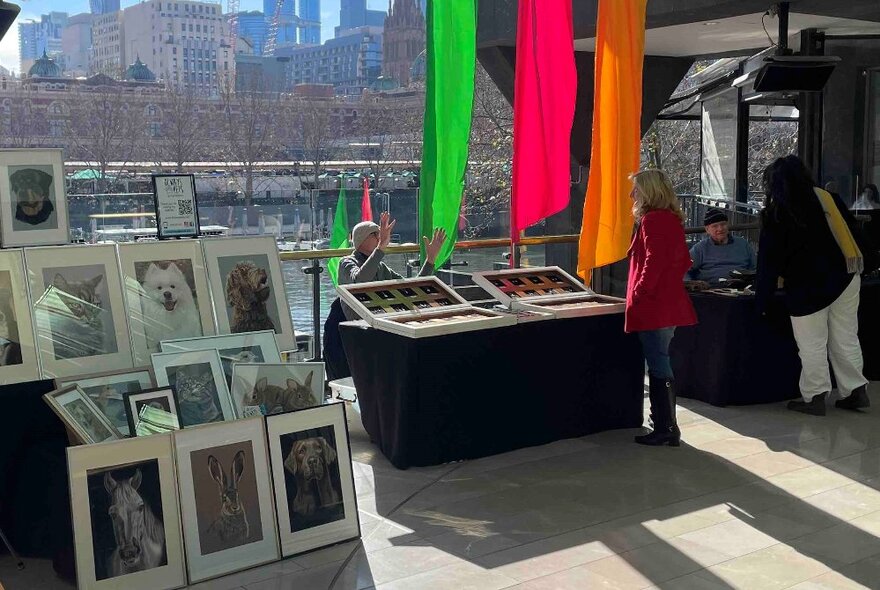 An outdoor market with artwork and prints for sale and three brightly coloured banners hanging down. 