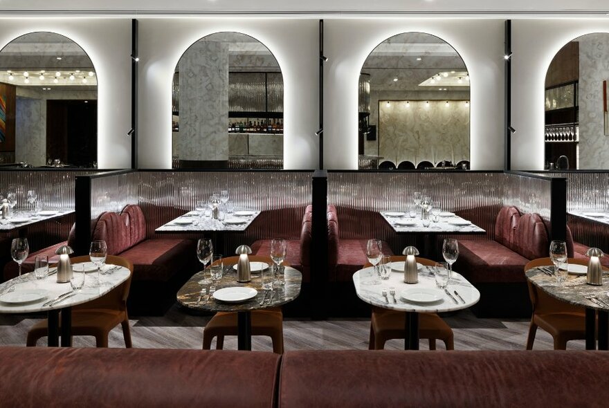 Dining room interior, with burgundy booths and arched mirrors at back wall, well set tables in foreground.