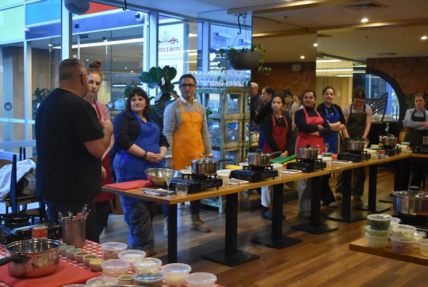 People standing at workstations with cooking equipment during a workshop.