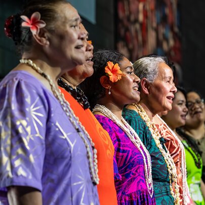 Pacific Islander people singing in a choir in tradition dress of varying bright colours.