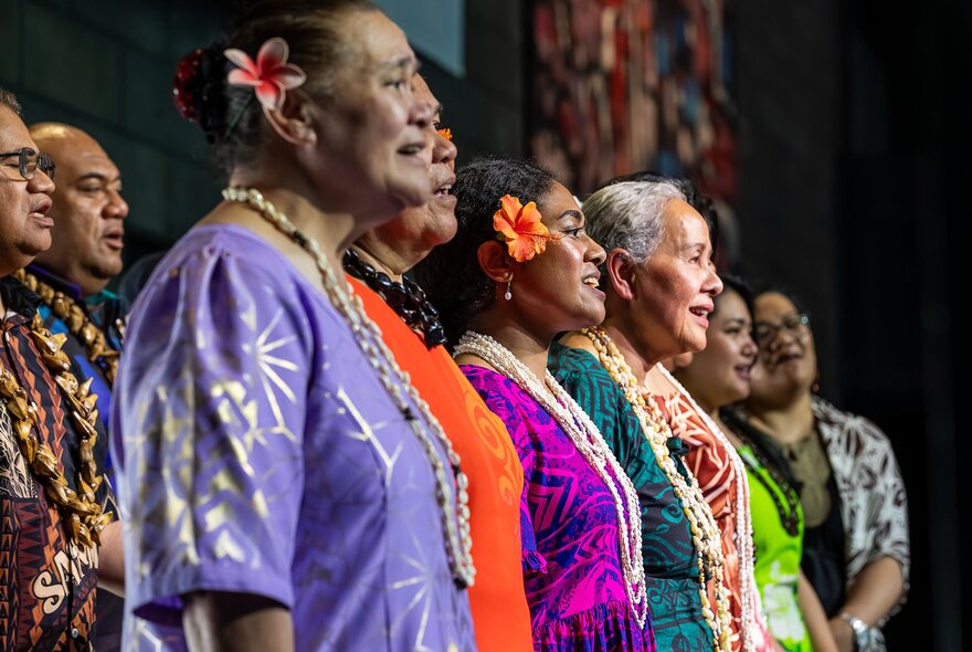 Pacific Islander people singing in a choir in tradition dress of varying bright colours.