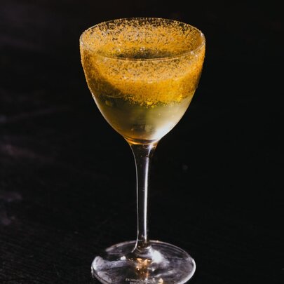 A cocktail in a mini martin glass, against a black background.