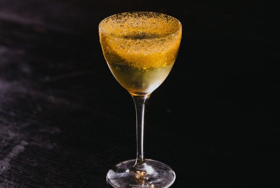 A cocktail in a mini martin glass, against a black background.