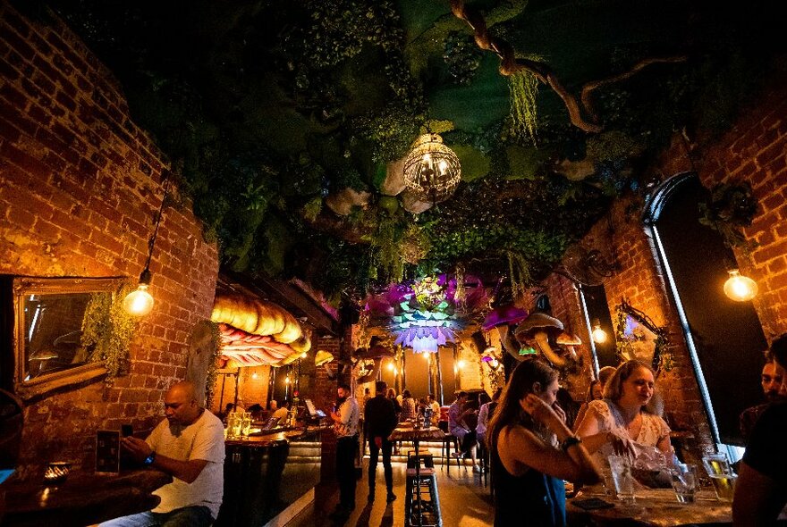 Noir cellar bar interior with people seated at tables by lamplight.