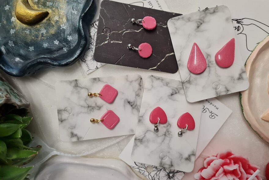 Pairs of pink polymer clay earrings attached to cards on a table.