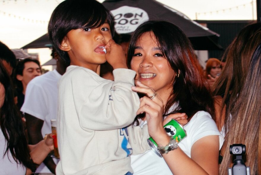 Woman holding a child on her shoulder, people in the background.