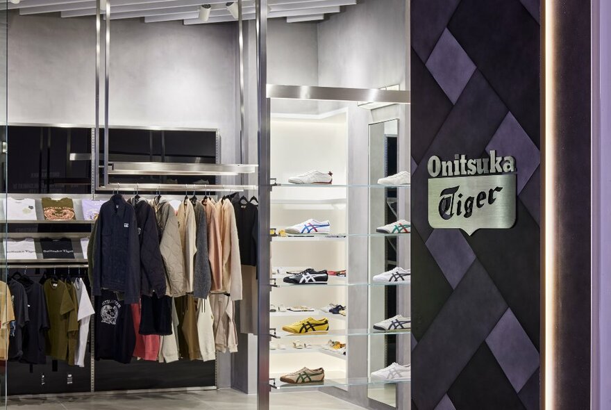 Clothing hanging on a rack next to shelving with colourful Onitsuka Tiger shoes in a flagship store. 