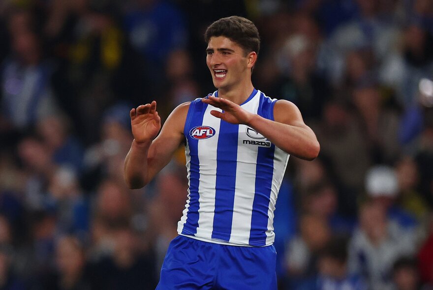 A North Melbourne AFL player cheering himself on the field with his arms raised to his chest.